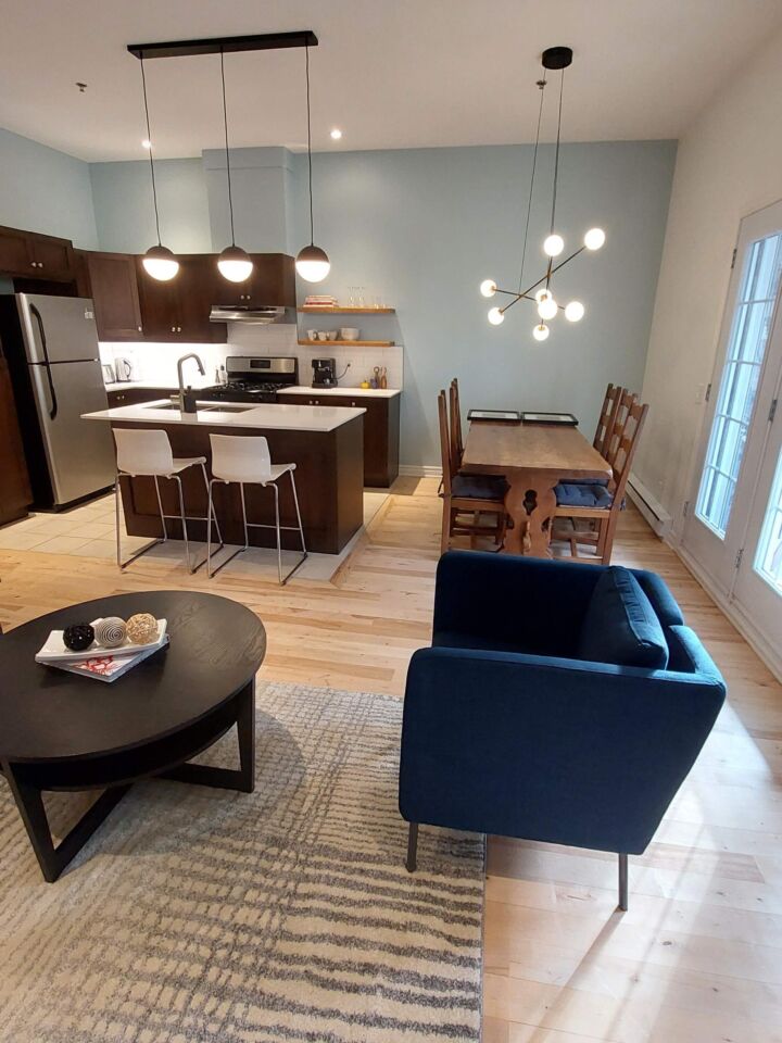 Coin salle à manger et cuisine ouverte avec armoires foncées et luminaires apparents, Résidence Verdet