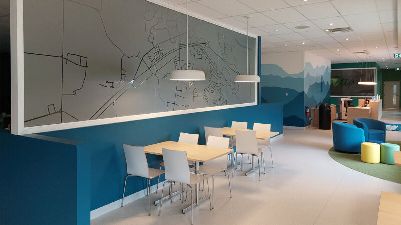 Salle principale avec tables mobiles, chaises blanches et murale cartographique, Centre communautaire de Bromont